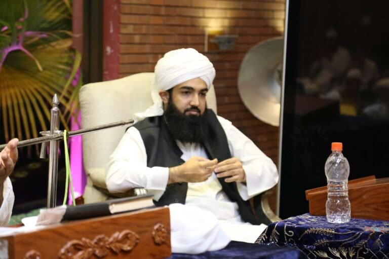 Shaykh Muhammad Bin Mohsin Mohsini, seated and engaged in a discussion (Majlis), wearing a traditional white turban and black vest, conveying spiritual wisdom to an audience.