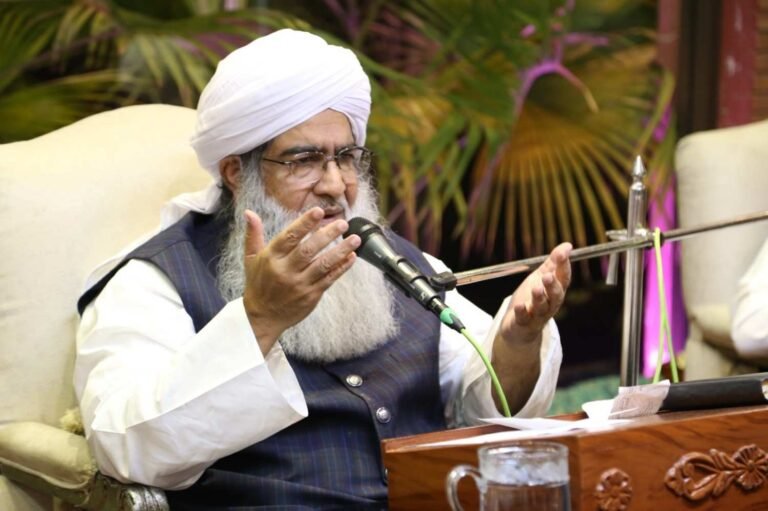 Shaykh Muhammad Mohsin Munawar Yousafi delivering a formal religious lecture into a microphone, wearing a white turban and vest, emphasizing traditional Islamic teachings.