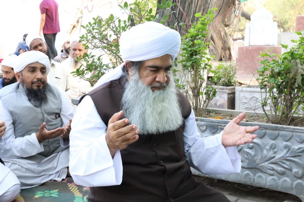 Shaykh Muhammad Mohsin Munawar Yousafi and another scholar seated outdoors, with hands raised in prayer (Dua), during a moment of spiritual contemplation at a holy site or graveyard.
